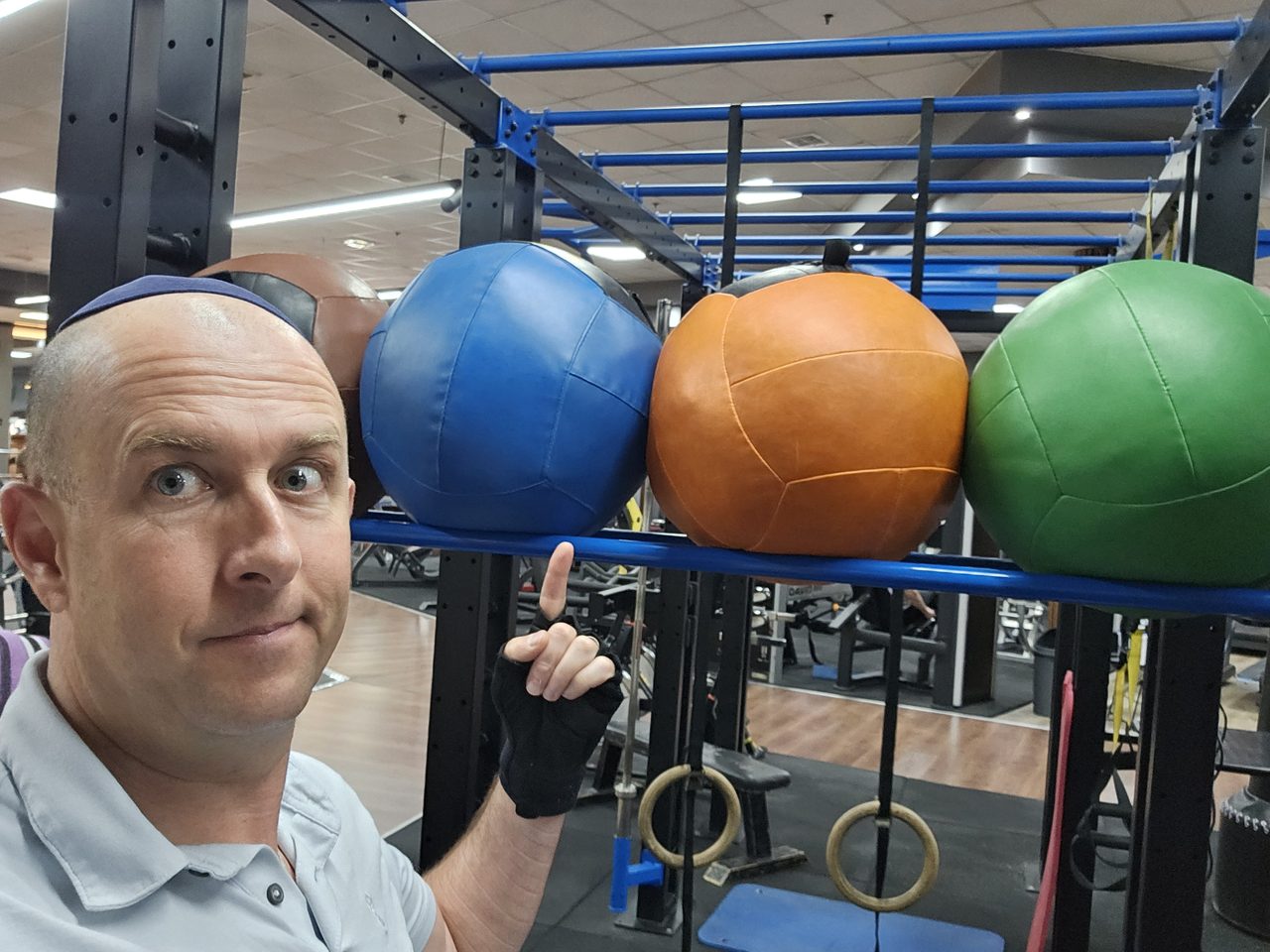 Tal Paperin pointing at medicine balls on a rack at the gym